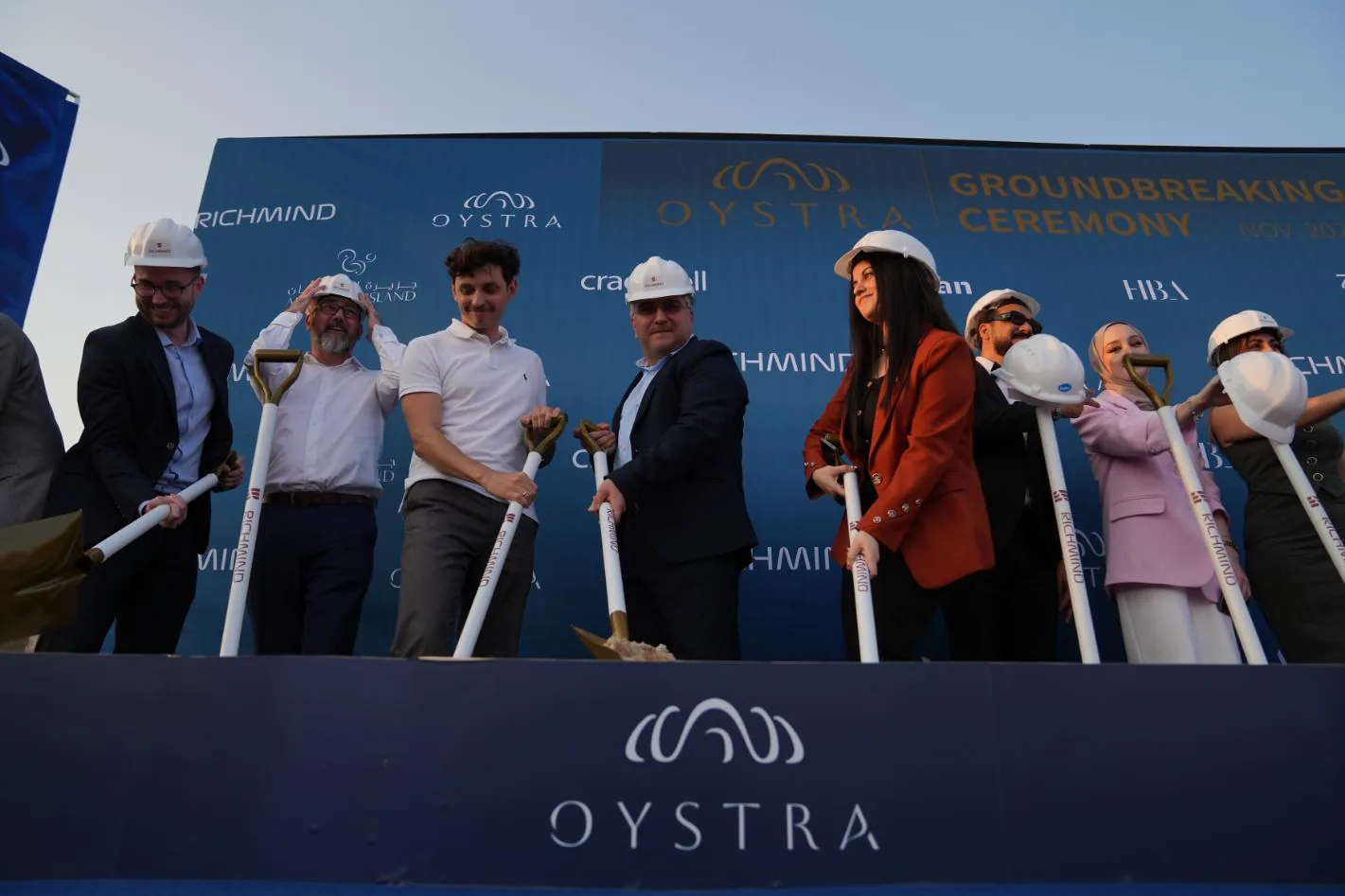 Guests in hard hats holding ceremonial shovels at the Oystra groundbreaking ceremony